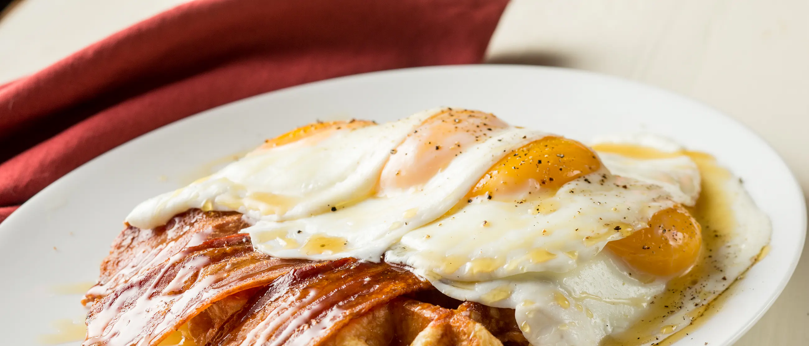 Maple syrup pouring over a Liège waffle topped with a sunny side up egg and bacon at Off The Waffle in downtown Eugene